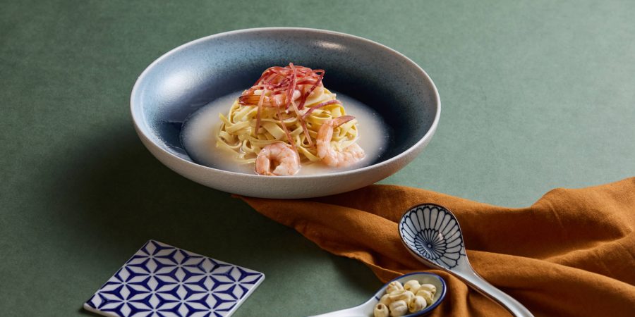 A closeup of a braised prawns dish with dried shredded tofu and Chinese ham. In front of the dish are two porcelain spoons and a coaster. 